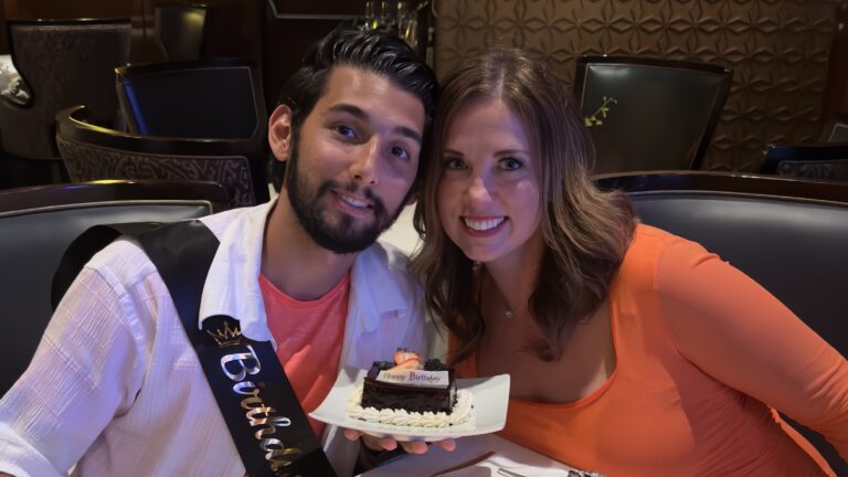 A couple at a dining table on a Holland America cruise ship celebrate a birthday with a piece of chocolate cake.