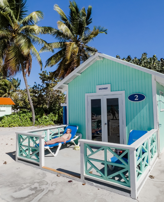 A light blue beach cabana with a sign that reads "GUINEP 2" stands against a clear blue sky.